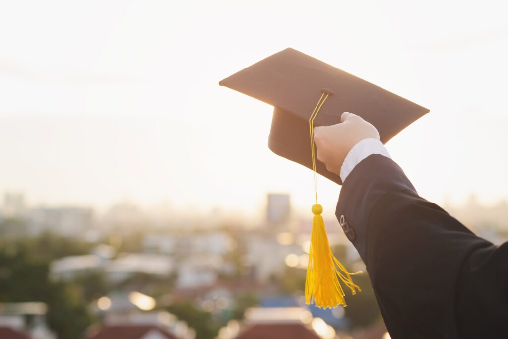 An arm holding up a graduation cap in the daylight